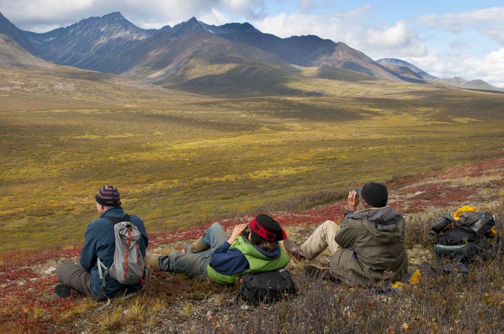 Three hikers resting on a hill overlooking mountains near Dechenla Wilderness Lodge in the NWT