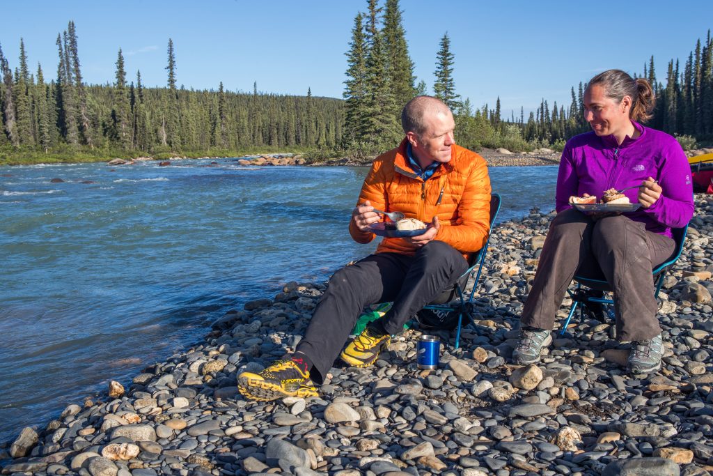 2 people eating a meal at the river's edge on a canoe trip in the Northwest Territories